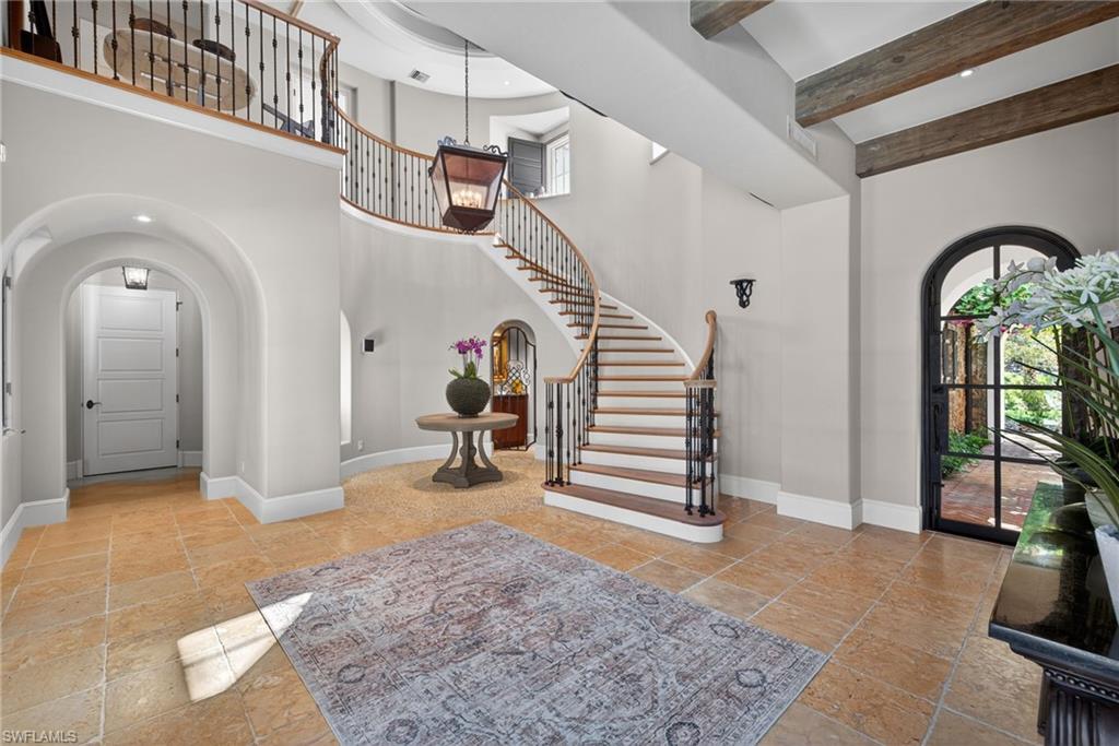 Foyer entrance with arched walkways, stairway, stone tile floors, beam ceiling, and recessed lighting