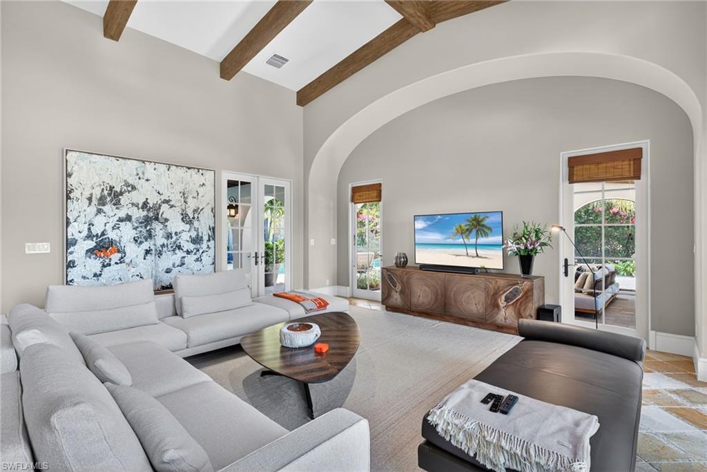 Living area featuring high vaulted ceiling, beamed ceiling, arched walkways, and stone tile floors