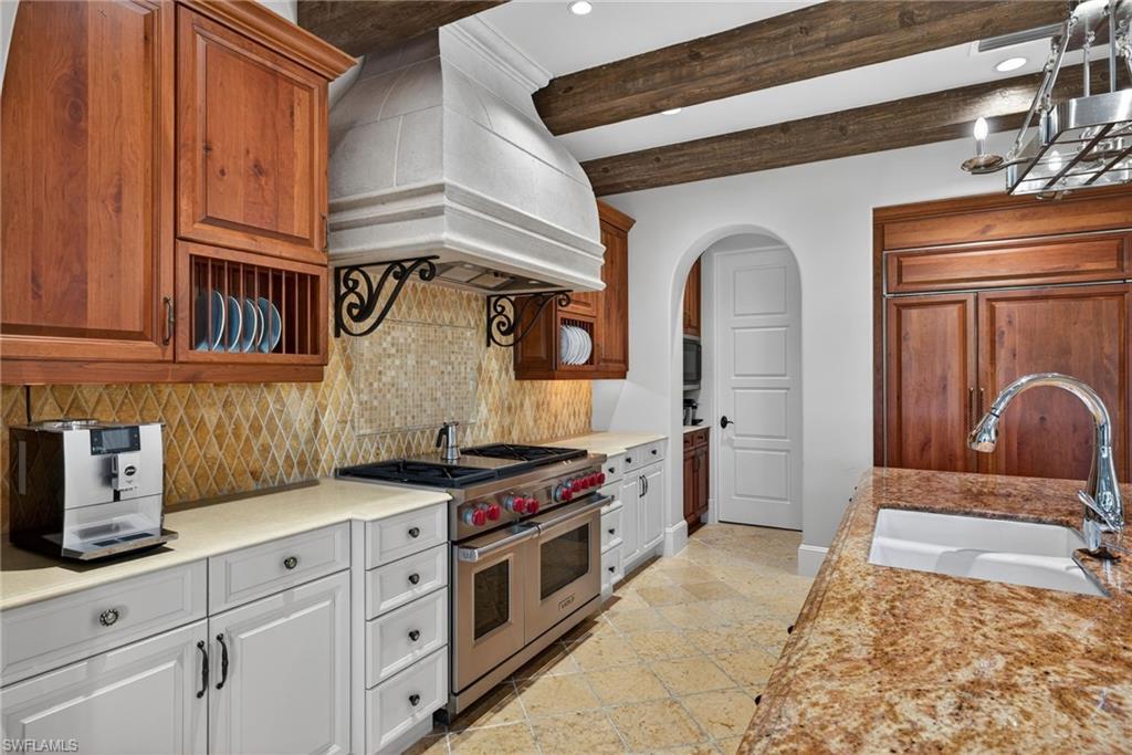 Kitchen with range with two ovens, arched walkways, backsplash, beamed ceiling, and exhaust hood