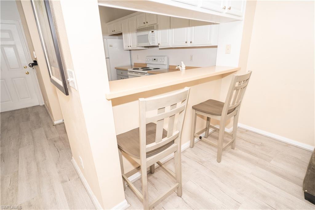 Kitchen with a kitchen breakfast bar, white appliances, light wood-style floors, and light countertops