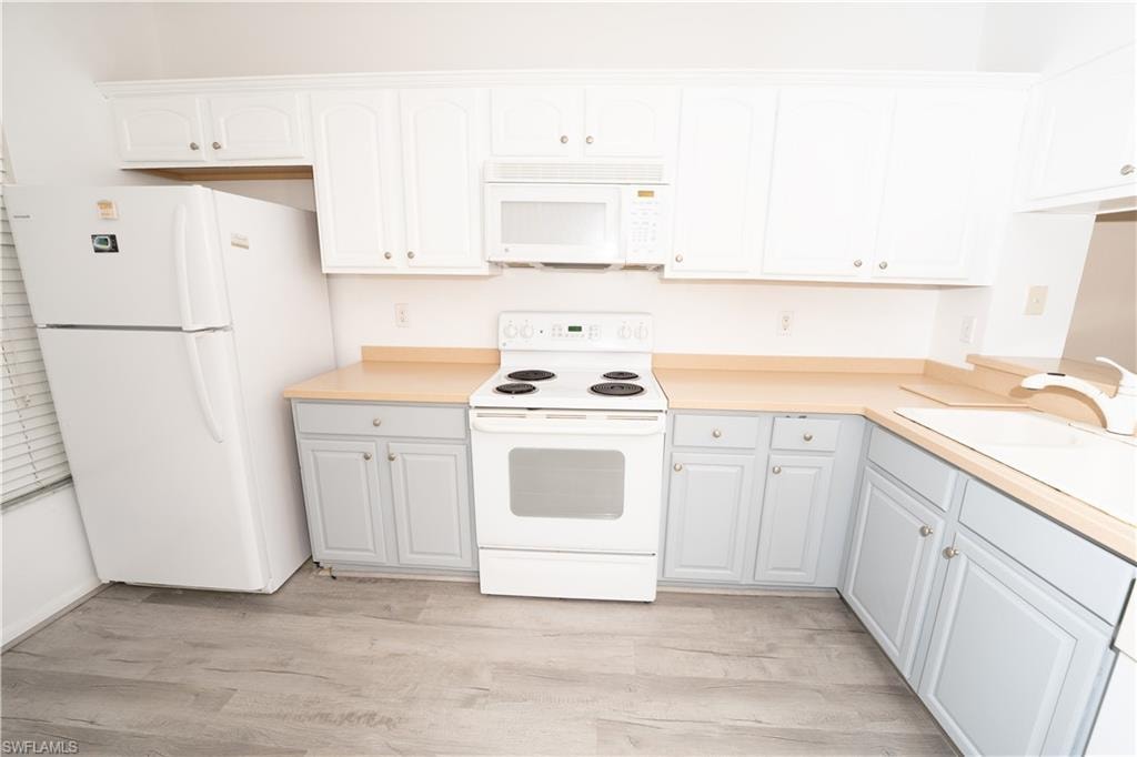 Kitchen featuring white appliances, light countertops, light wood finished floors, and white cabinetry