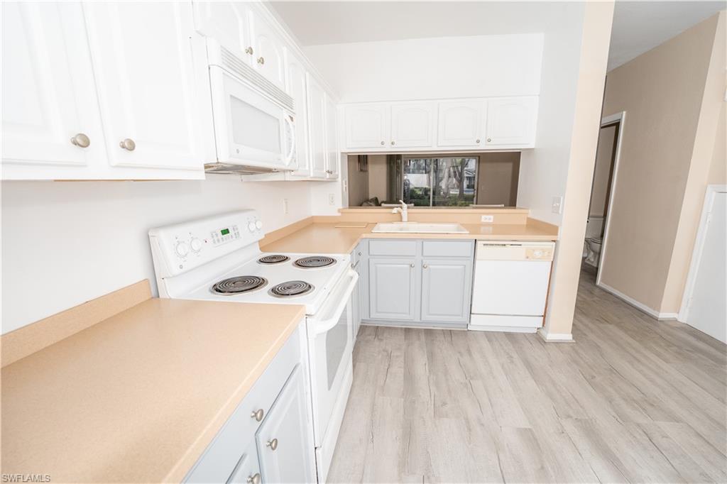 Kitchen featuring white appliances, white cabinetry, light countertops, and light wood finished floors