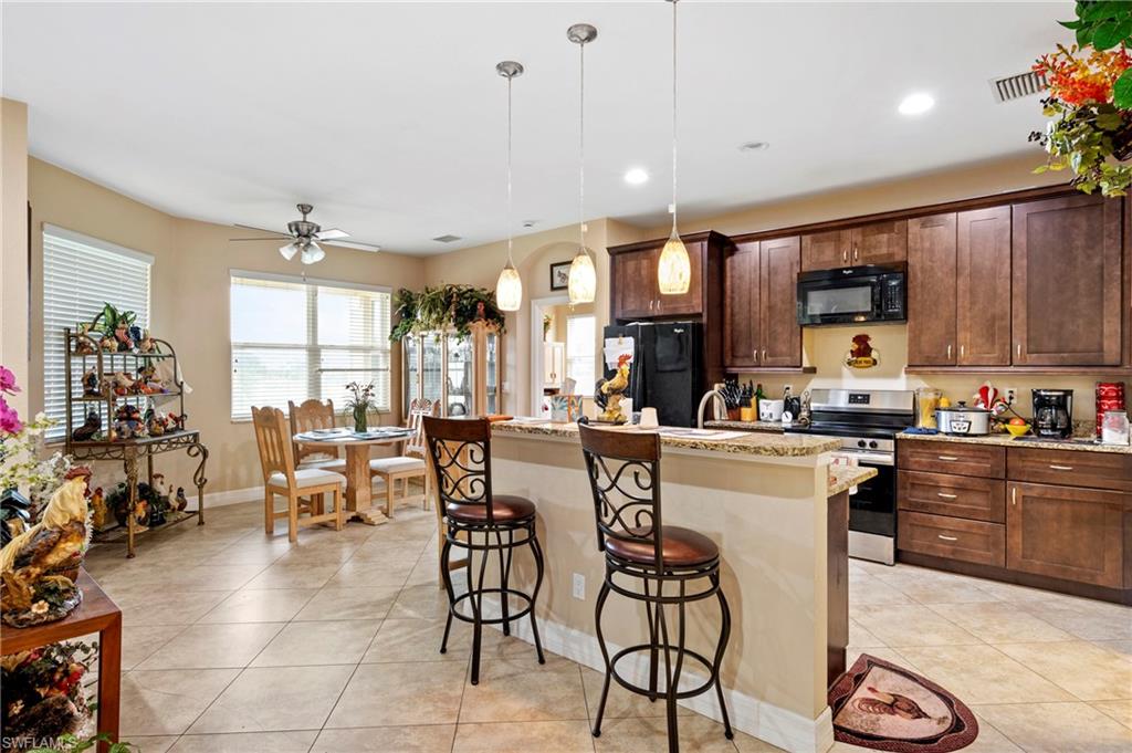 Kitchen with a kitchen bar, light tile patterned floors, black appliances, dark brown cabinetry, and recessed lighting