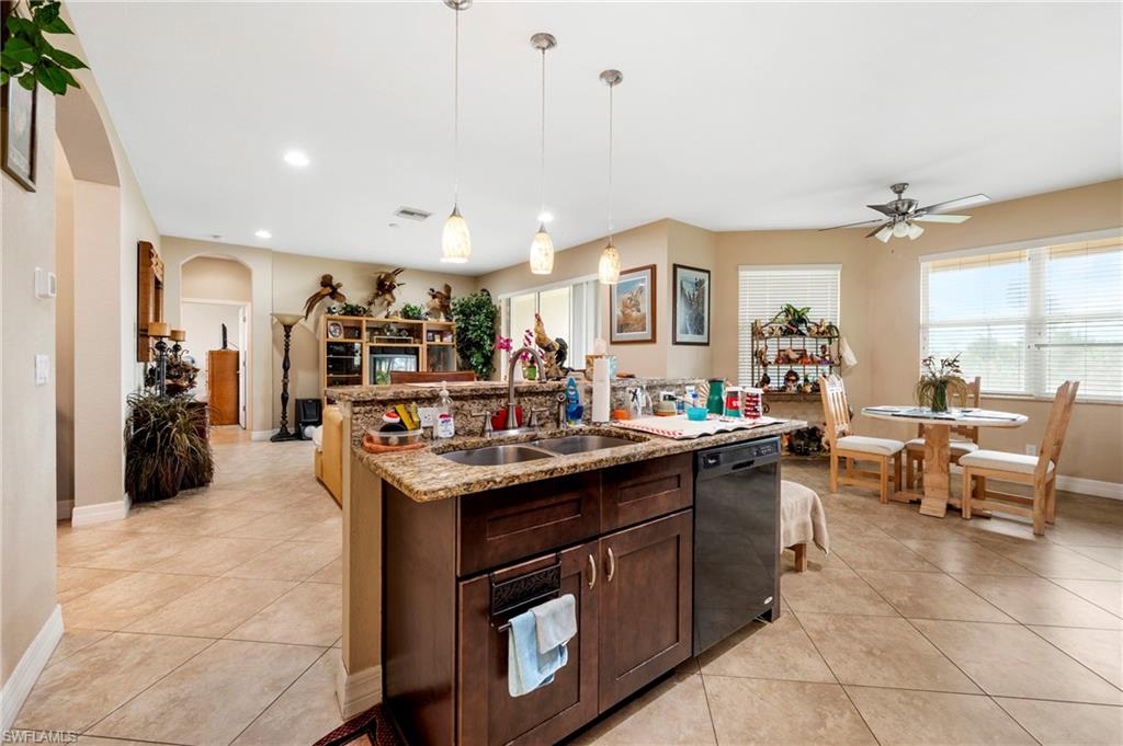 Kitchen with dark brown cabinetry, arched walkways, pendant lighting, light stone counters, and an island with sink
