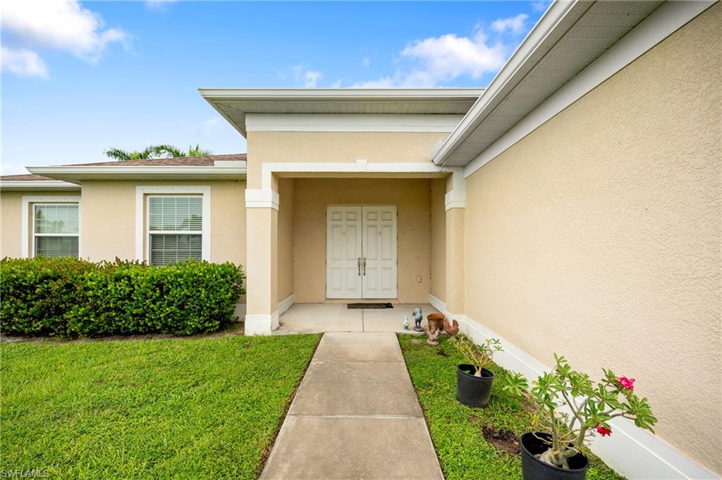 Entrance to property with stucco siding and a lawn