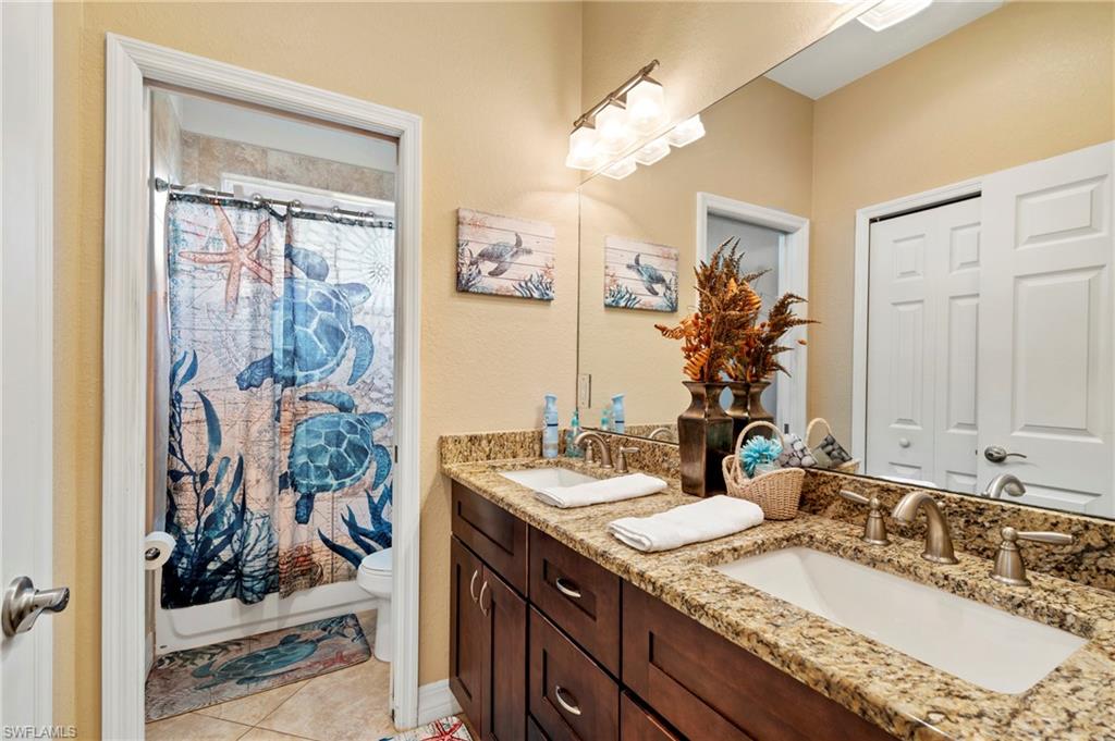 Full bath with double vanity, light tile patterned floors, and shower / tub combo with curtain