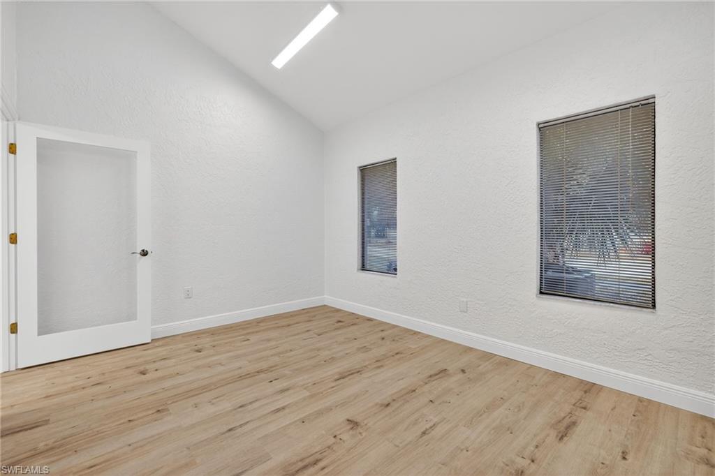 Spare room with vaulted ceiling, light wood finished floors, and a textured wall