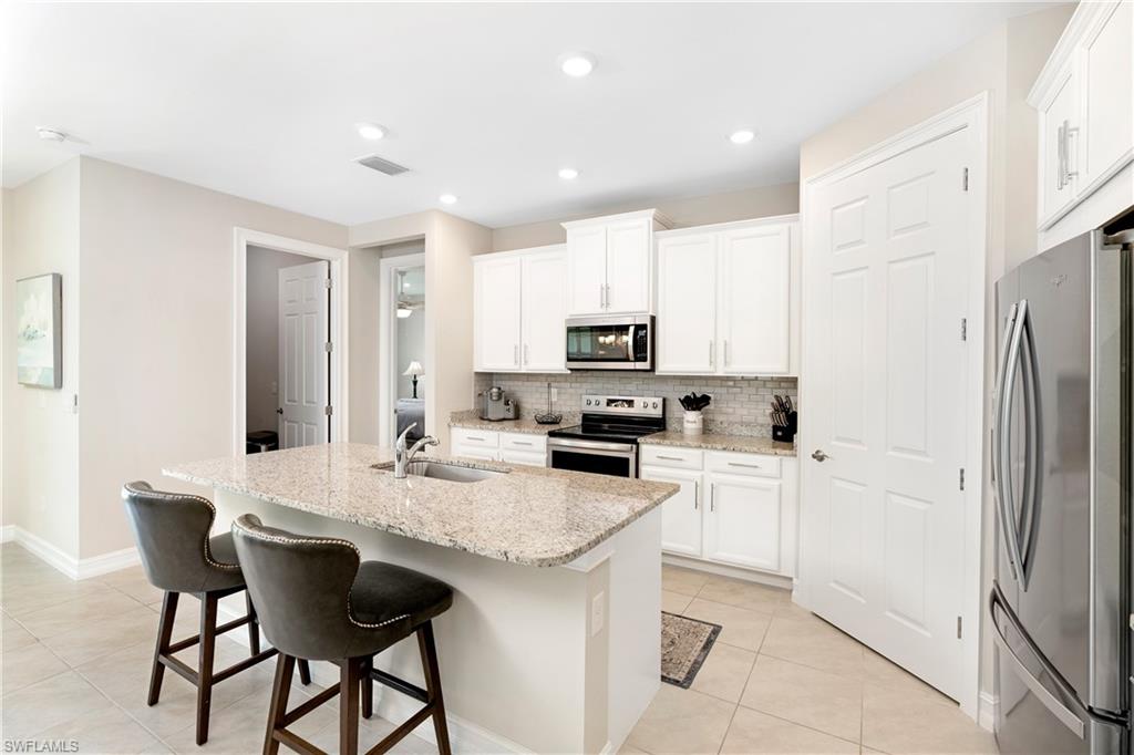 Kitchen featuring stainless steel appliances, light tile patterned floors, an island with sink, white cabinets, and recessed lighting
