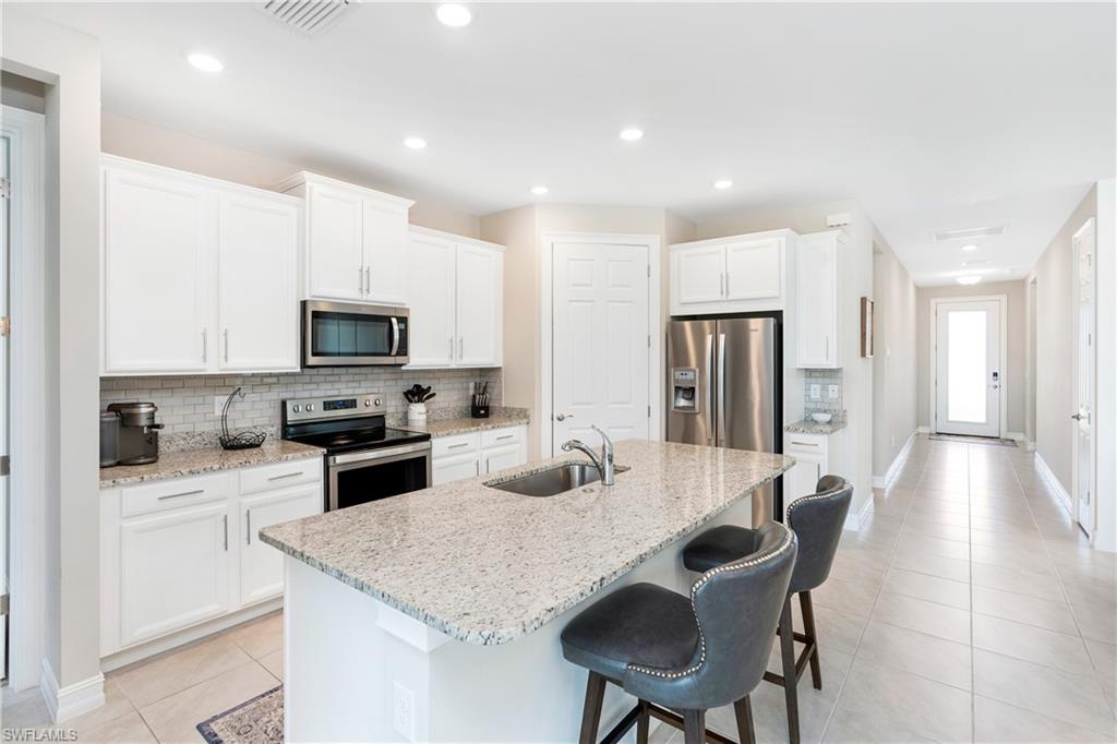 Kitchen with stainless steel appliances, white cabinetry, tasteful backsplash, light stone counters, and light tile patterned floors