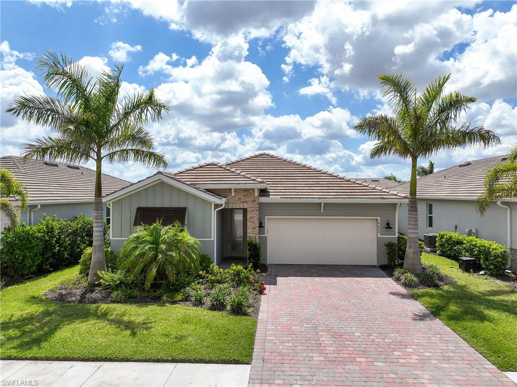 Single story home featuring a front yard, stone siding, a tile roof, and decorative driveway