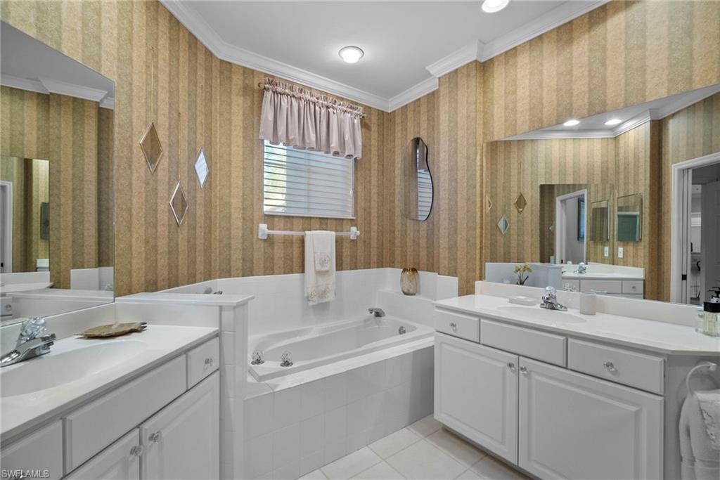 Full bathroom featuring wallpapered walls, a garden tub, two vanities, light tile patterned flooring, and ornamental molding