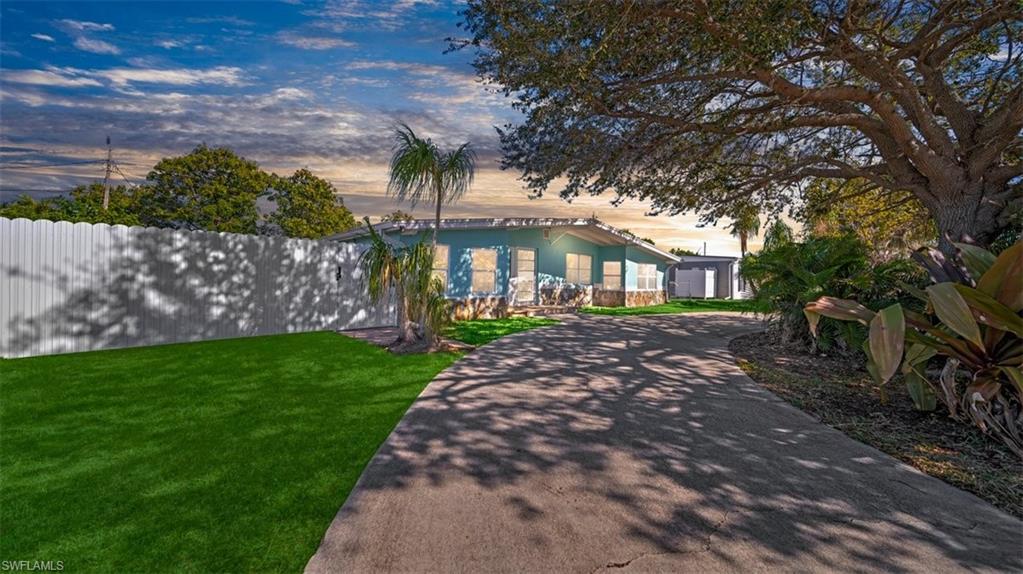 View of property hidden behind natural elements featuring a lawn, driveway, and an outbuilding