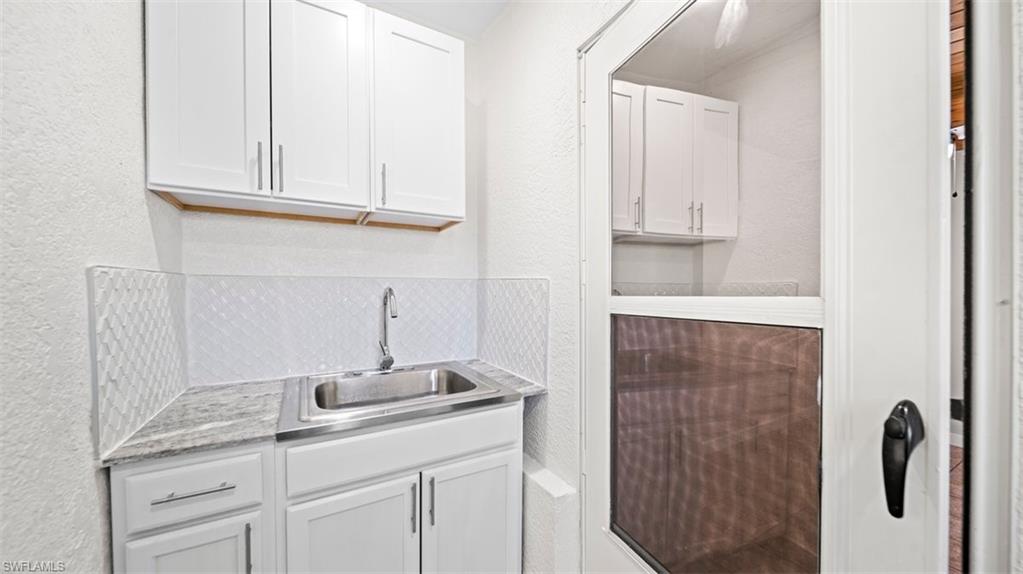 Bar area featuring a textured wall, white cabinetry, light countertops, and tasteful backsplash