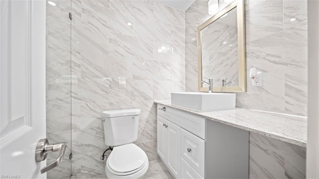 Bathroom featuring tile walls, vanity, and light marble finish flooring