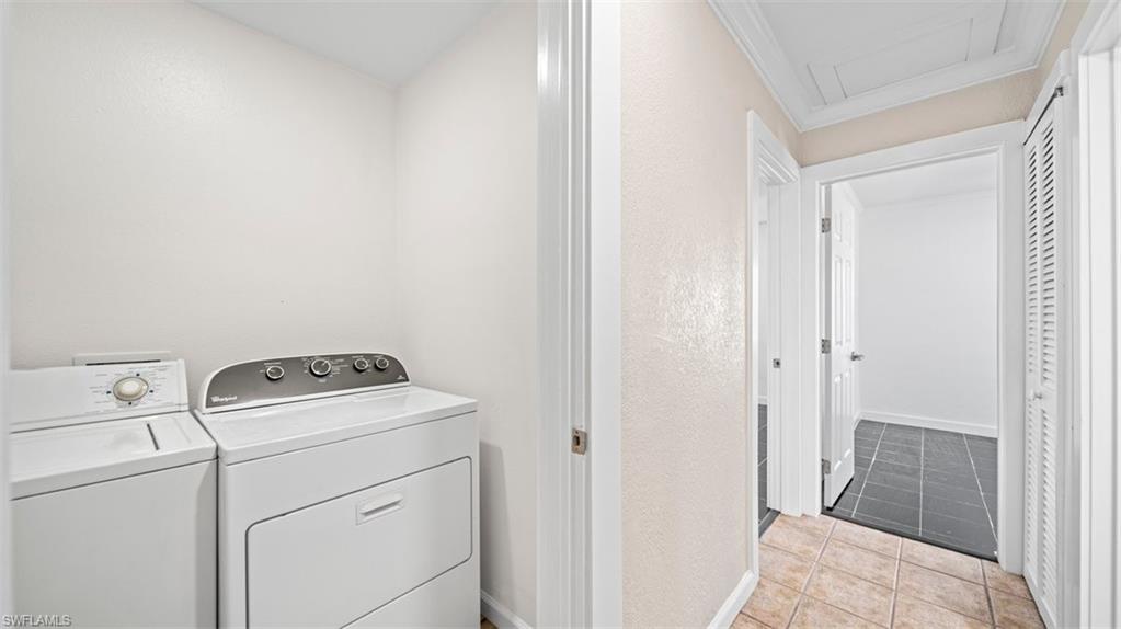 Laundry room featuring light tile patterned floors, separate washer and dryer, and a textured wall