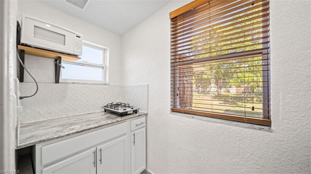 Kitchen featuring a textured wall, white microwave, light stone counters, white cabinets, and tasteful backsplash