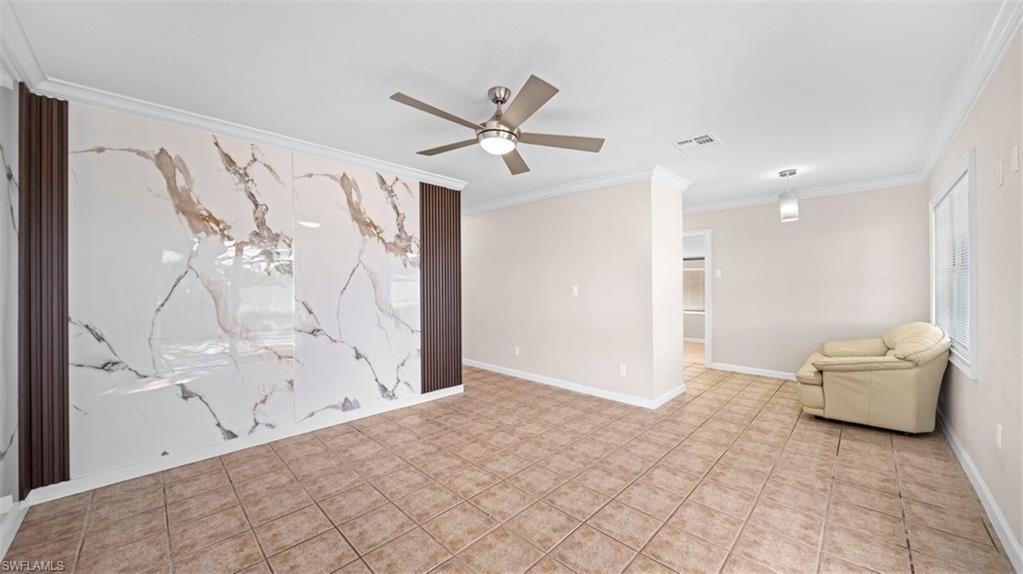 Tiled spare room featuring a ceiling fan, crown molding, and an accent wall