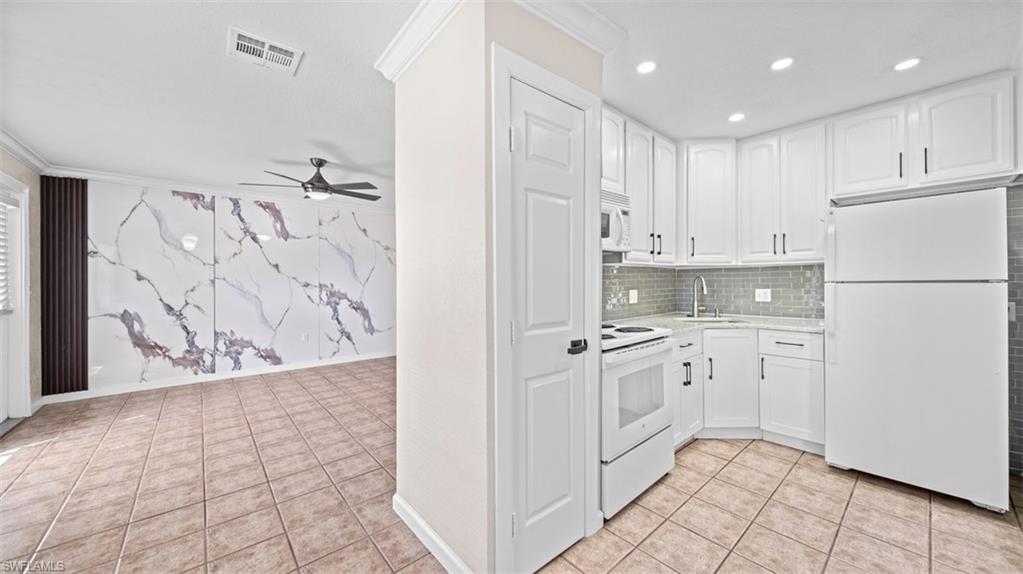 Kitchen with white appliances, ornamental molding, light tile patterned floors, white cabinetry, and a ceiling fan
