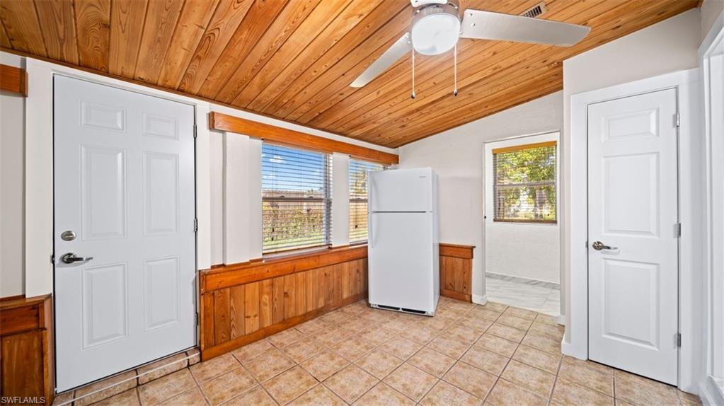 Kitchen featuring wooden ceiling, vaulted ceiling, freestanding refrigerator, healthy amount of natural light, and wooden walls