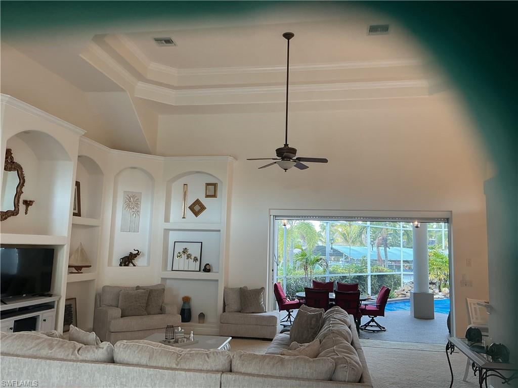 Living room with built in features, ceiling fan, crown molding, a raised ceiling, and a sunroom