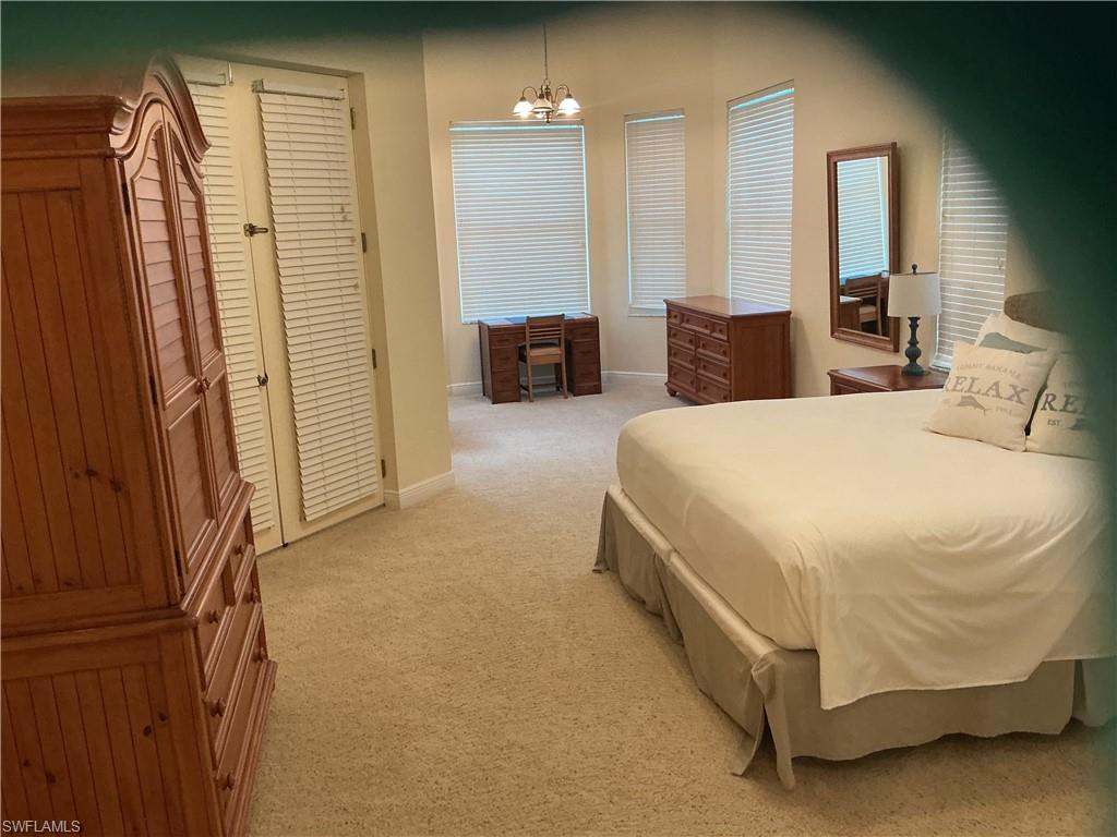 Bedroom with light colored carpet, a chandelier, and a desk