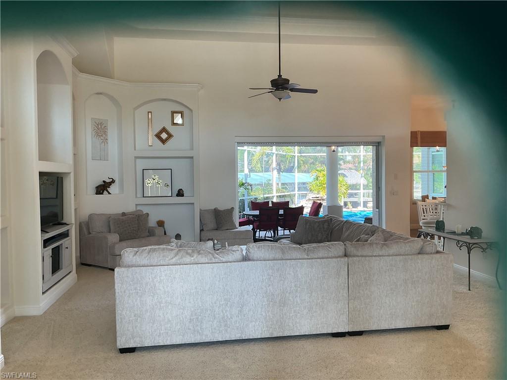 Living area with a ceiling fan, a high ceiling, light colored carpet, and built in features