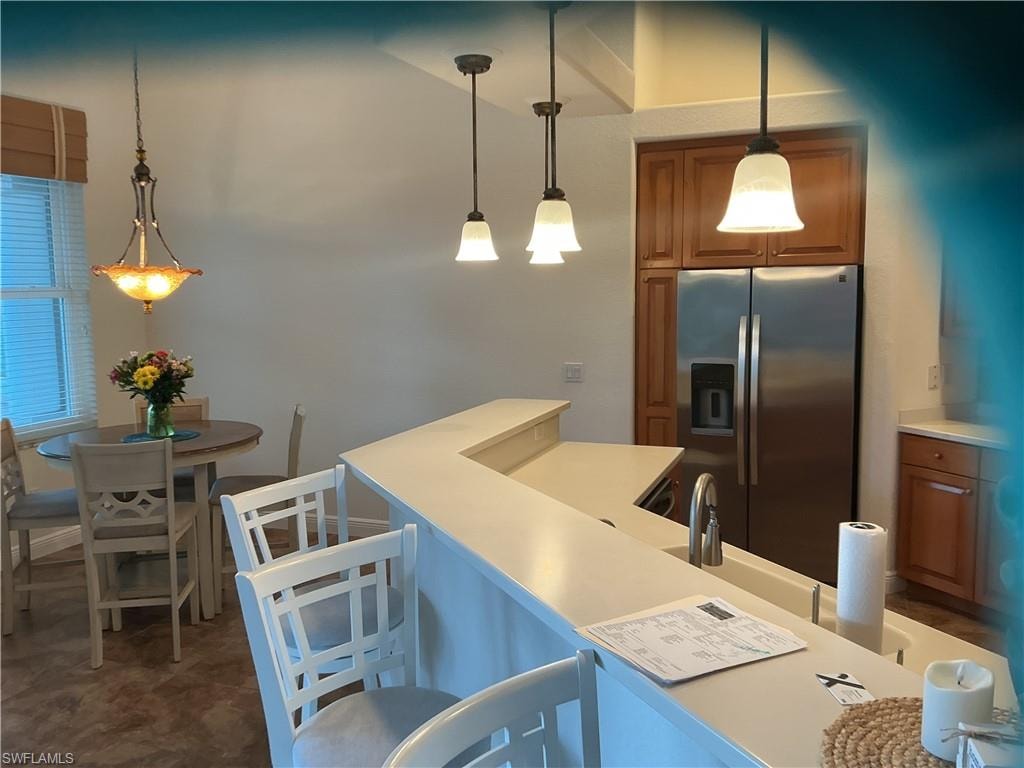 Kitchen featuring wood finish cabinetry, stainless steel fridge, light countertops, and a breakfast bar