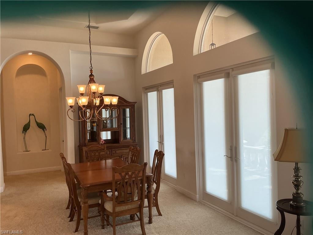 Dining area with light carpet, suspended lighting, and a high ceiling