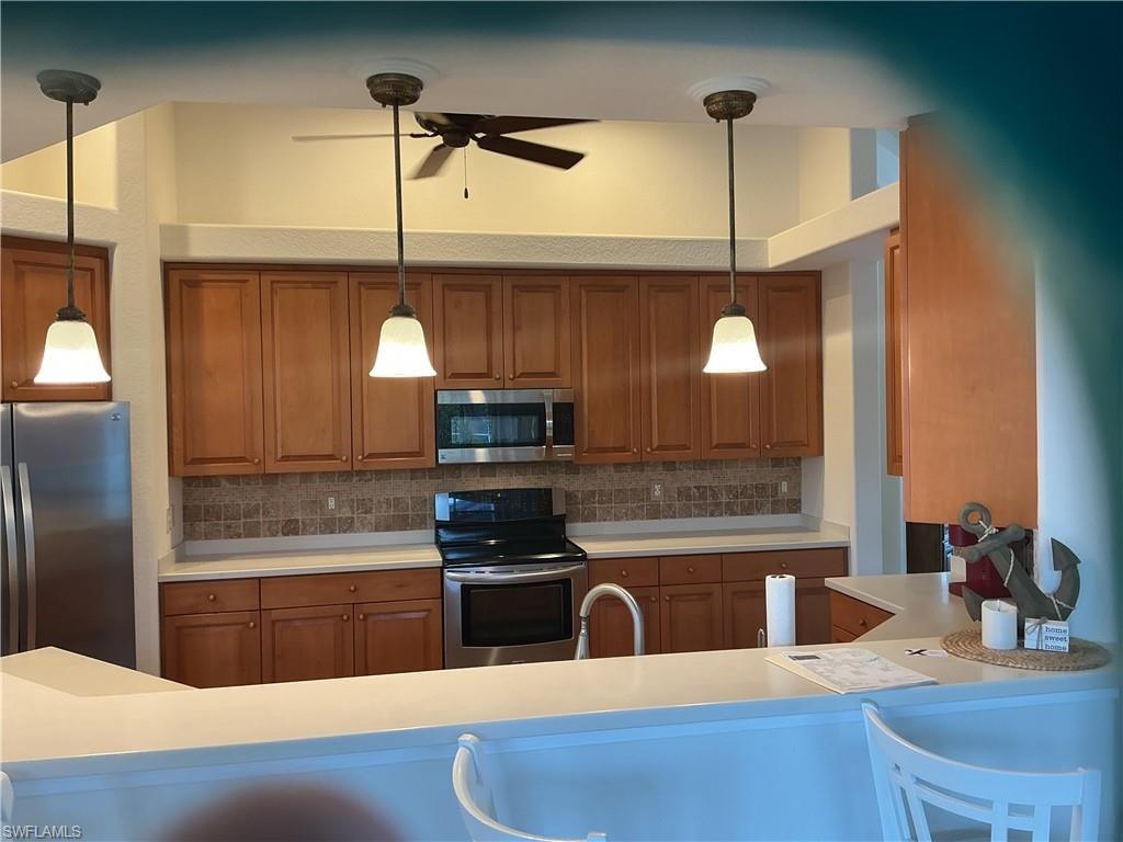 Kitchen with wood finish cabinetry, light countertops, stainless steel appliances, and pendant lighting