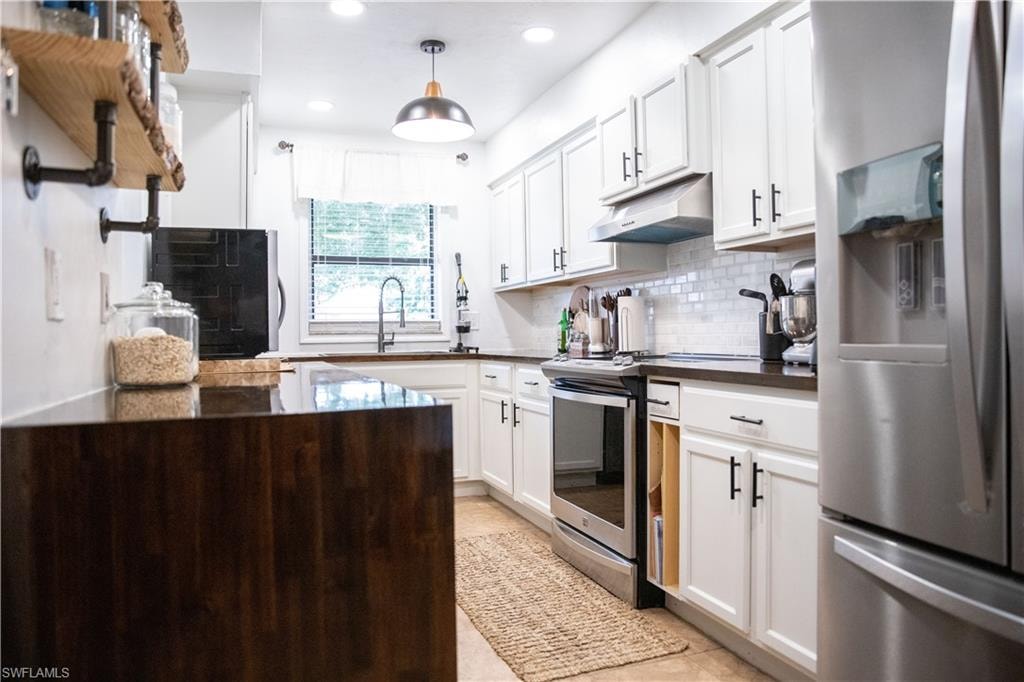 Kitchen with appliances with stainless steel finishes, backsplash, white cabinets, under cabinet range hood, and recessed lighting