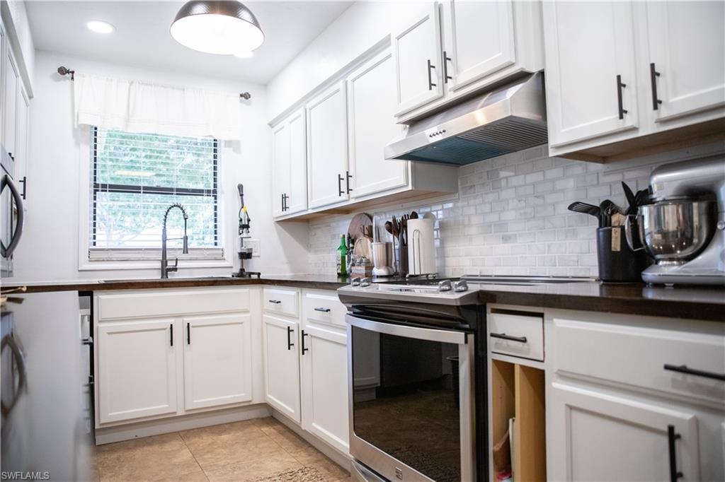 Kitchen with gas stove, under cabinet range hood, white cabinets, tasteful backsplash, and light tile patterned floors