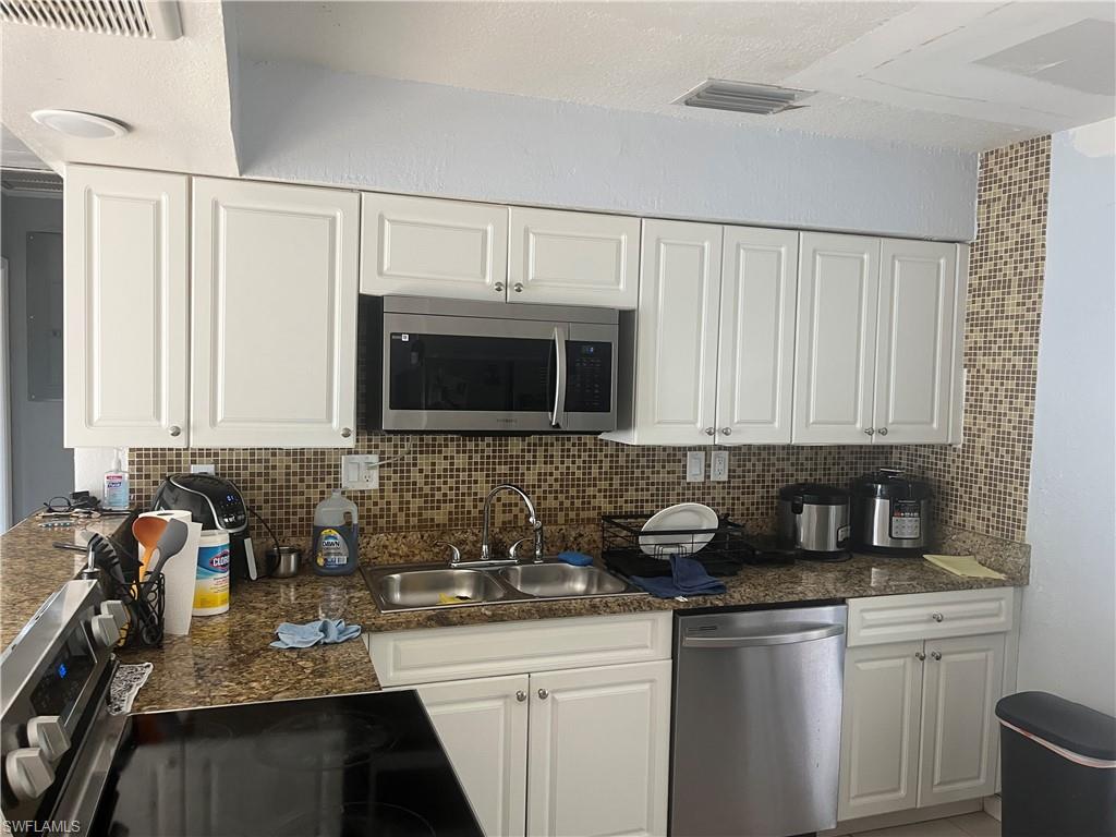 Kitchen with stainless steel appliances, white cabinetry, backsplash, and dark stone countertops