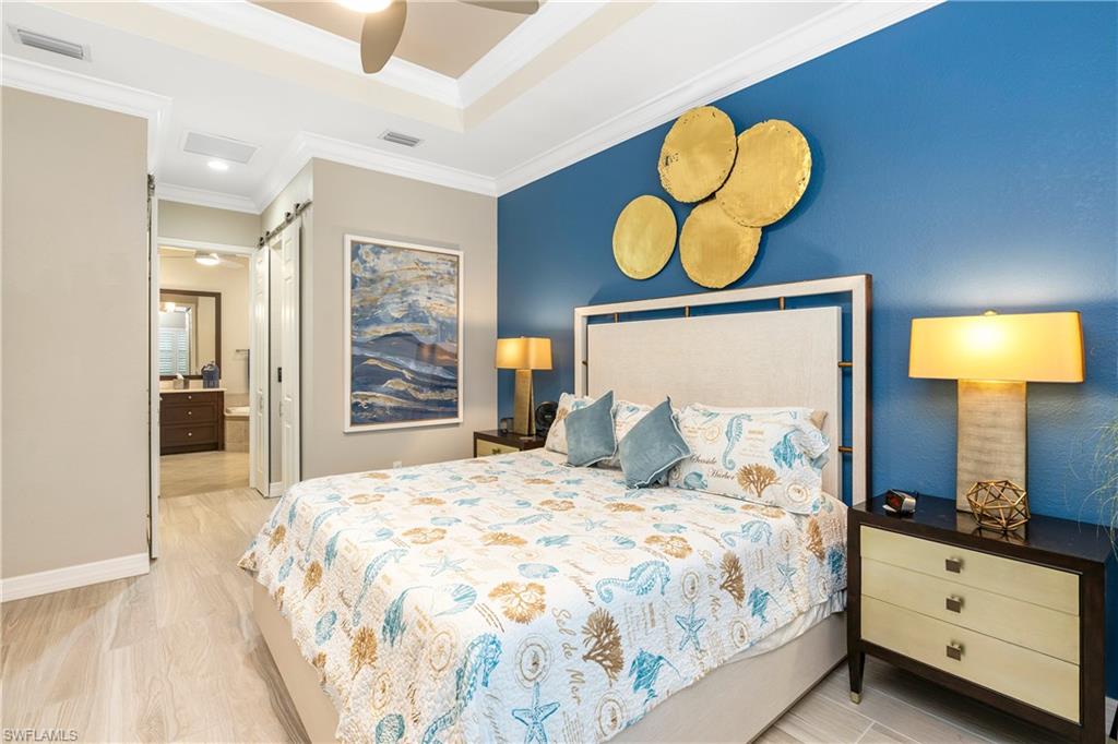 Bedroom featuring a barn door, light wood-style floors, crown molding, a ceiling fan, and a closet