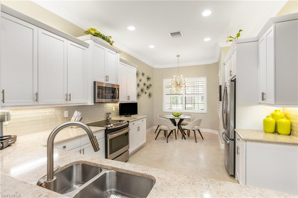 Kitchen with backsplash, ornamental molding, white cabinets, appliances with stainless steel finishes, and light stone countertops