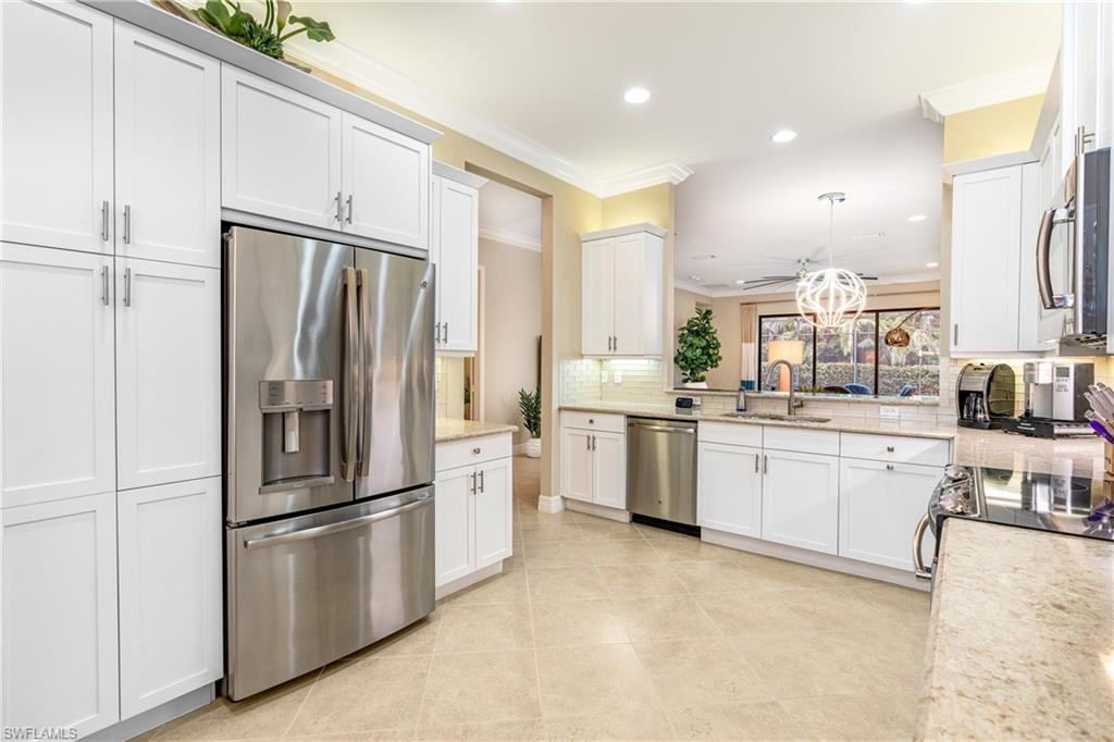 Kitchen with crown molding, appliances with stainless steel finishes, white cabinetry, pendant lighting, and decorative backsplash