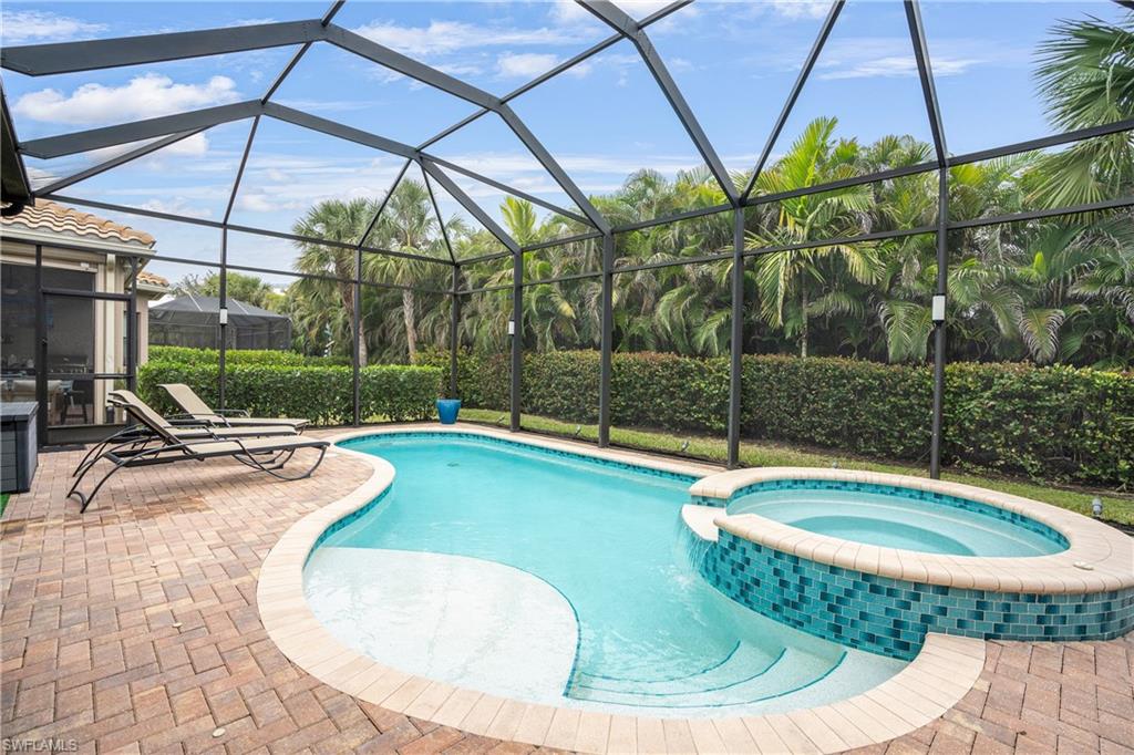 View of pool featuring a pool with connected hot tub, a sunroom, a patio, and glass enclosure
