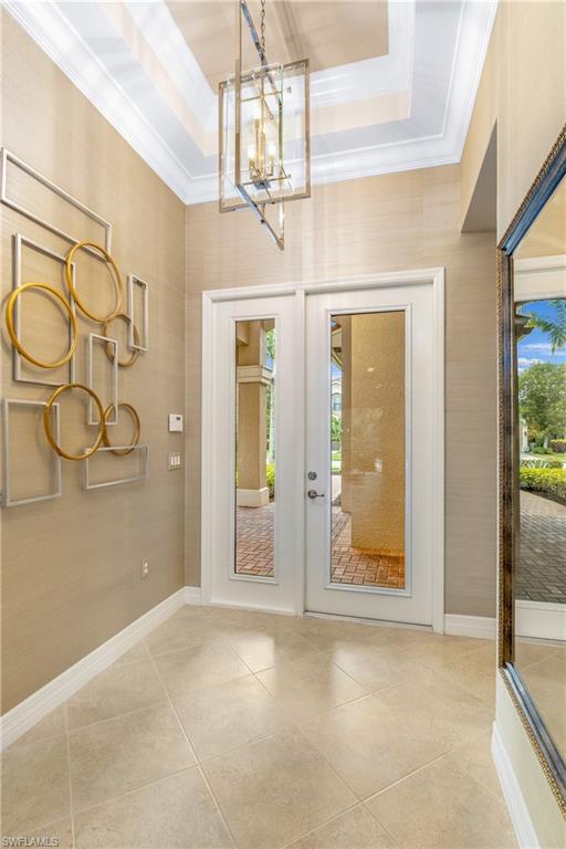 Foyer entrance featuring a raised ceiling, a chandelier, french doors, and crown molding