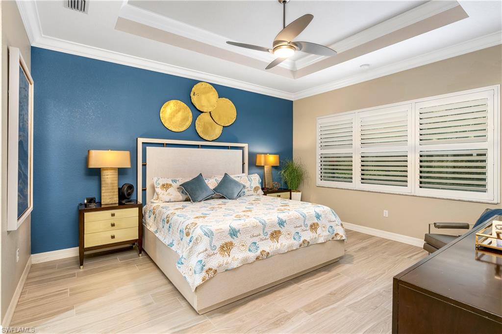 Bedroom with wood finish floors, a raised ceiling, ornamental molding, and a ceiling fan