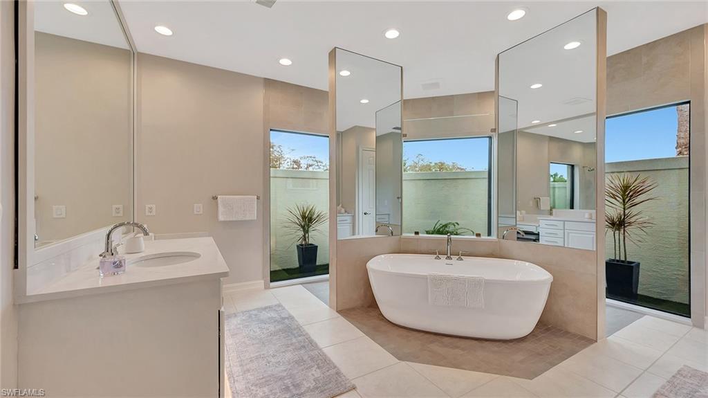 Primary Bathroom featuring a soaking tub, his and hers vanities, and a glass walled walk-in shower.