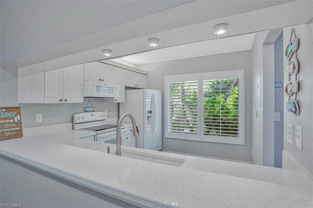 Kitchen with white appliances, white cabinets, and light stone counters