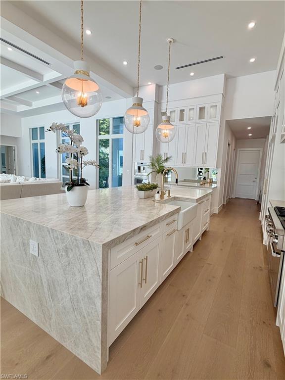 Kitchen with light stone counters, white cabinets, light wood-style flooring, hanging light fixtures, and beamed ceiling