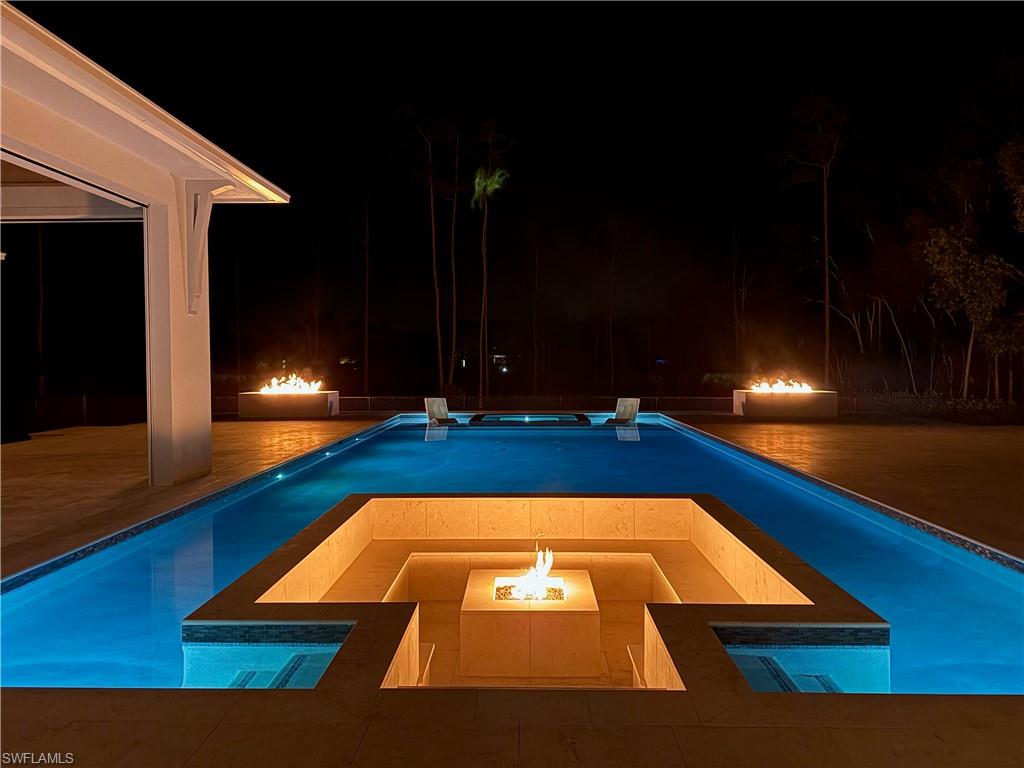 Pool at twilight featuring a fire pit, an outdoor pool, an in-ground hot tub, and a patio area