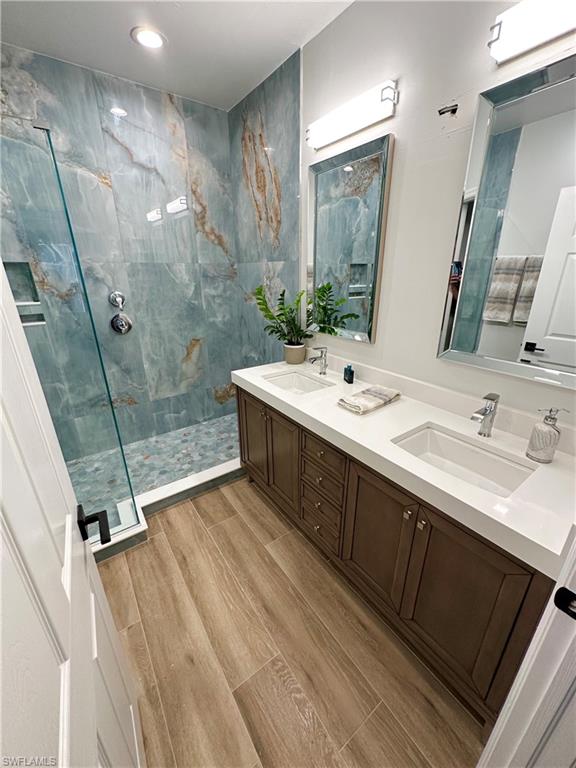 Full bath with a marble finish shower, double vanity, wood finish floors, and recessed lighting