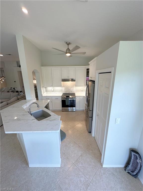 Kitchen featuring stainless steel appliances, white cabinets, light stone countertops, light tile patterned flooring, and open floor plan