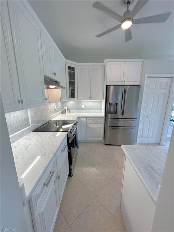 Kitchen with stainless steel appliances, glass insert cabinets, white cabinetry, light stone counters, and under cabinet range hood