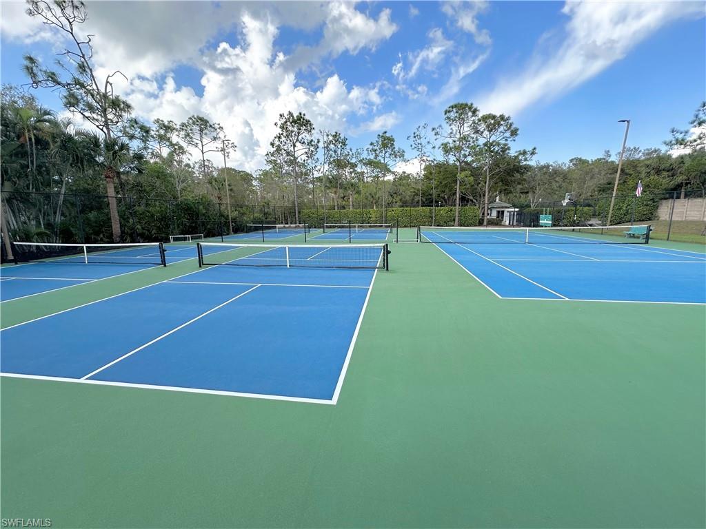 View of tennis court featuring community basketball court and view of wooded area