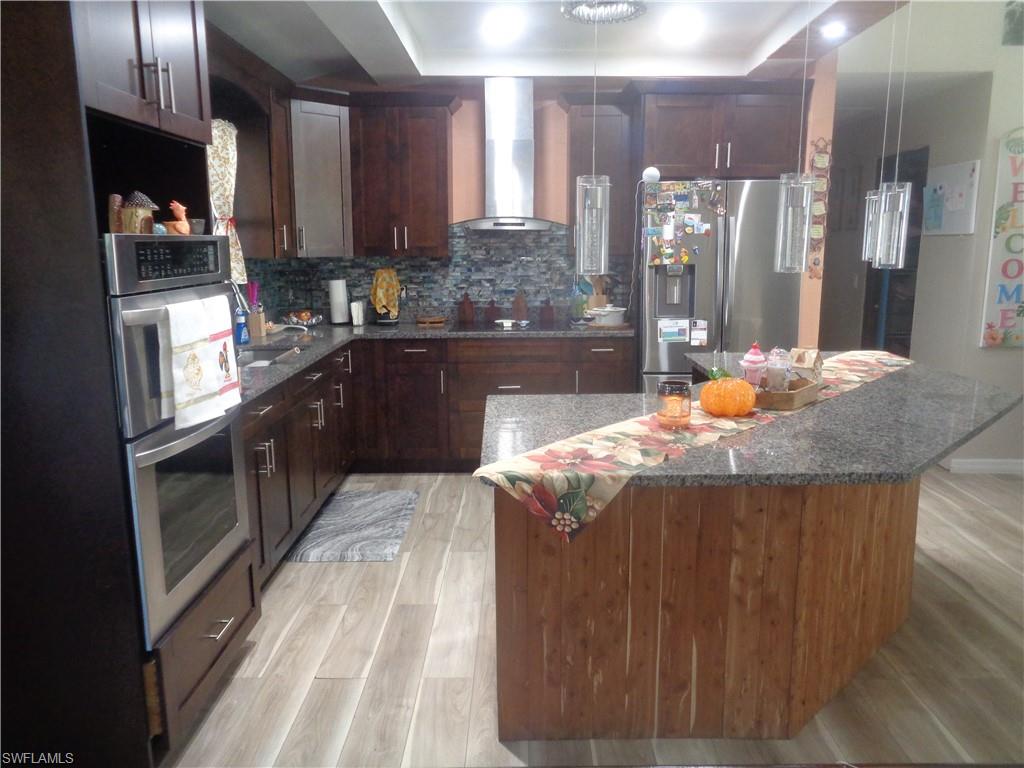 Kitchen with wall chimney range hood, stainless steel appliances, granite counters, light wood finished floors, and dark brown cabinets