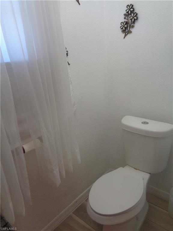 Master bedroom's bathroom toilet with baseboards and wood finished floors