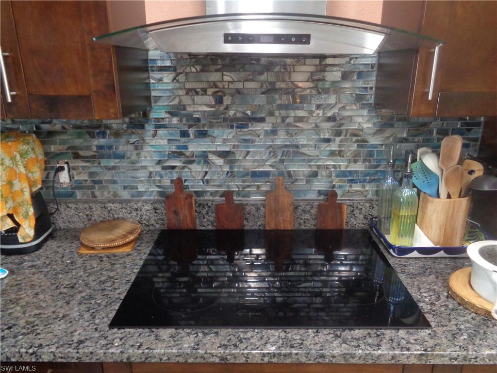 Kitchen view of ventilation hood, backsplash, black electric stovetop, and granite counters