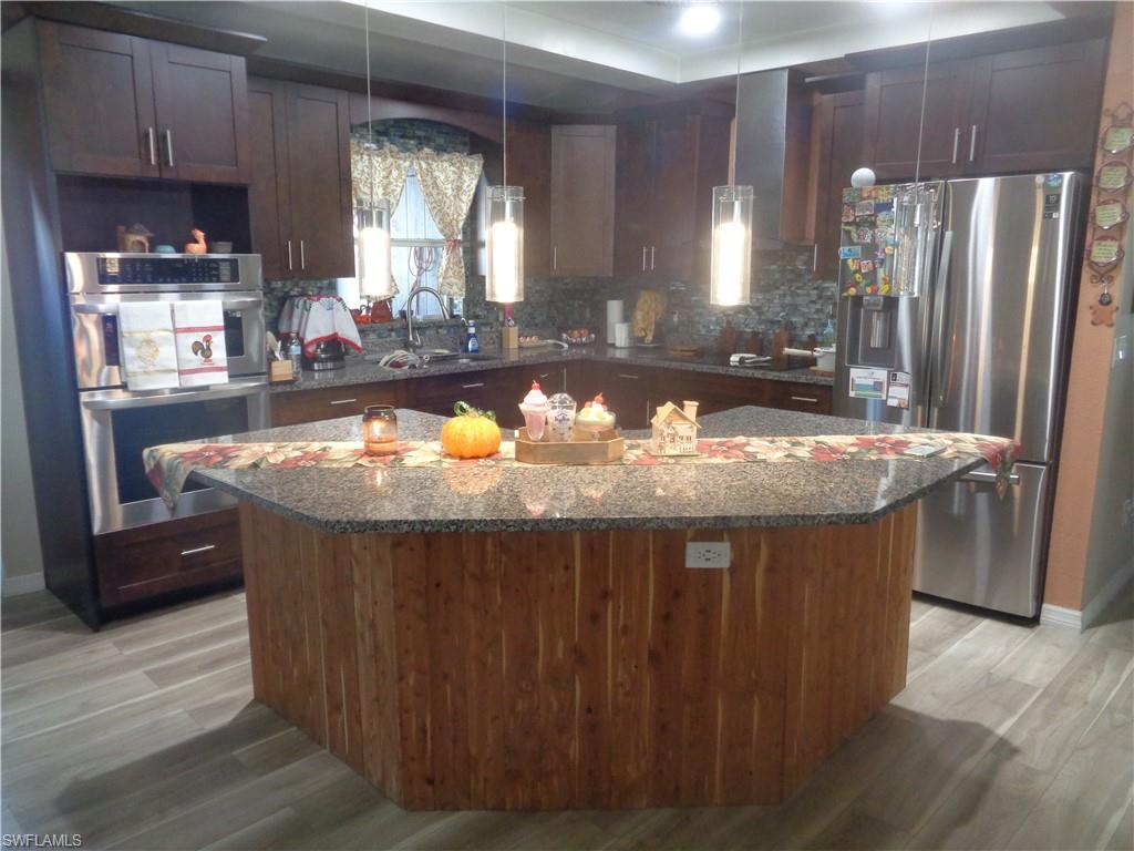 Kitchen with appliances with stainless steel appliances, dark brown cabinetry, granite countertops, a kitchen island, and light wood-style flooring